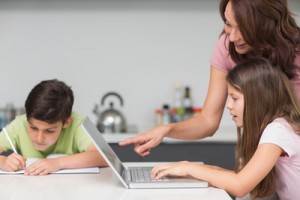 Side view of a mother with young kids using laptop in the kitchen at home